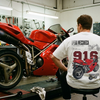 T-shirt moto Opera Meccanica 916 porté de dos dans un atelier, face à une Ducati 916 rouge