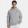 Homme portant un hoodie gris clair TOURISMO avec un pantalon blanc sur fond neutre