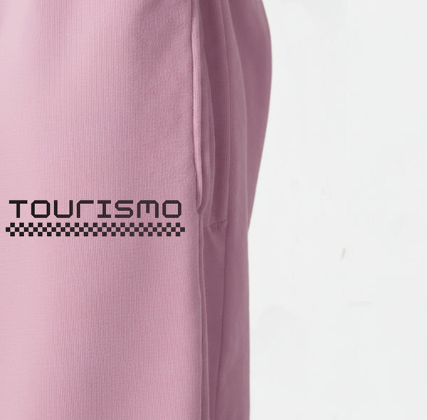 Gros plan sur le logo "Tourismo" blanc imprimé sur le pantalon de jogging rose.