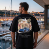 Homme portant le t-shirt noir Aero Estate 911 GT3 RS sur une terrasse de marina au crépuscule entre yachts