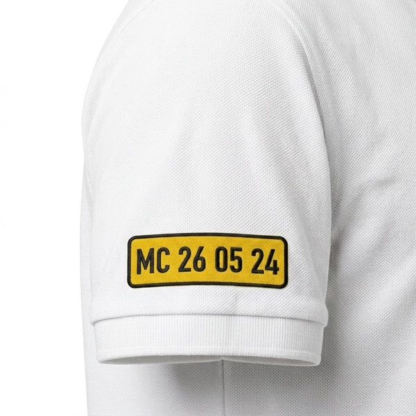 Gros plan sur la plaque MC 26 05 24 brodée sur la manche du polo blanc