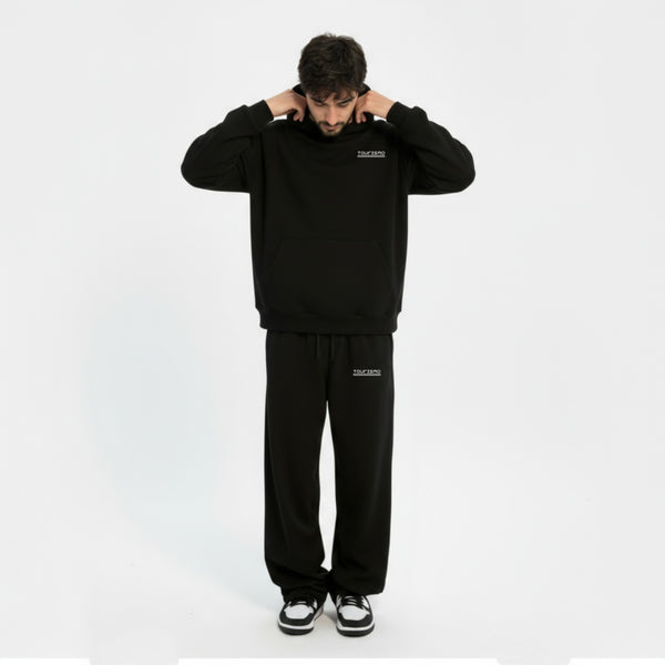 Homme portant un ensemble noir TOURISMO, tirant sur sa capuche en regardant vers le bas