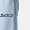 Gros plan sur le logo "Tourismo" blanc imprimé sur le pantalon de jogging bleu ciel.